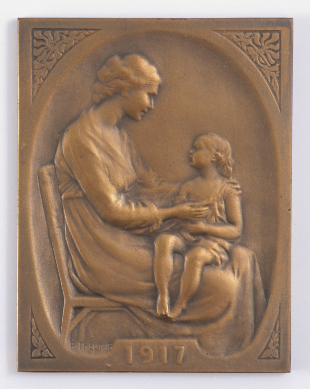 Eine Bronzetafel, die eine Frau mit sanftem Gesichtsausdruck zeigt, die auf einem Stuhl sitzt und ein zufriedenes Kind in den Armen hält, mit der Inschrift "Mutter und Kind".