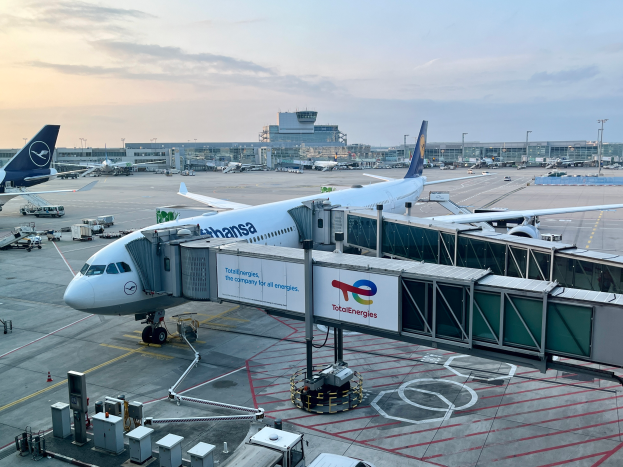 Ein großes Passagierflugzeug auf einem Flughafenvorfeld umgeben von anderen Flugzeugen, Fahrzeugen und Gebäuden unter einem klaren blauen Himmel.