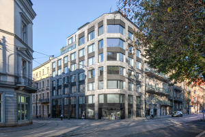 Großes mehrstöckiges Bürogebäude mit zahlreichen Fenstern, umgeben von Straßeninfrastruktur, Fahrzeugen, Fußgängern, Bäumen und einem bewölkten Himmel.