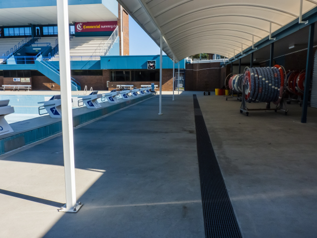 Ein großes Hallenbad an der University of Texas at Austin, umgeben von Stühlen, mit Objekten rechts, Pfählen links und einem Gebäude mit Treppen, Geländern und Texttafeln im Hintergrund.