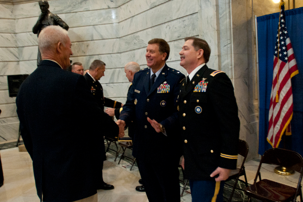 Leute schütteln sich die Hände vor Stühlen, mit einer Statue, Flagge und Vorhang im Hintergrund.