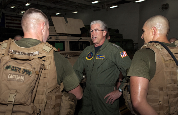 Eine Gruppe von Männern in Militäruniformen, die vor einer beleuchteten Wand diskutieren, mit einem Kommandeur in der Mitte.