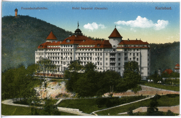 Alte Postkarte des Hotel Imperial in Karlsbad, Deutschland, das ein großes Gebäude mit Fenstern zeigt, umgeben von Bäumen, Pflanzen, einem Weg, Hügeln und einem bewölkten Himmel, mit Text oben.