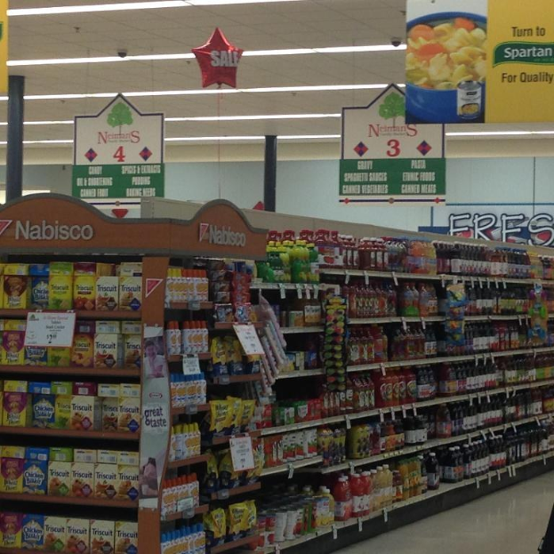 Ein Supermarktinneres mit deckenmontierten Lampen und Schildern, auf denen Lebensmittel auf Regalen zu sehen sind.