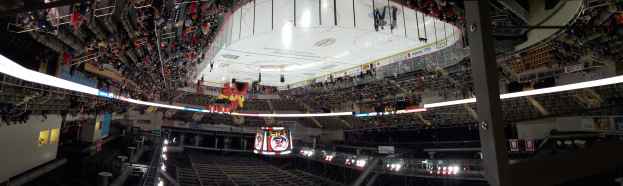 Eine große Arena voller Zuschauer bei einem Hockey-Spiel, mit Stühlen, Geländern, Tafeln mit Text, Lampen, Pfosten und Treppen, die zum Sitzbereich führen.