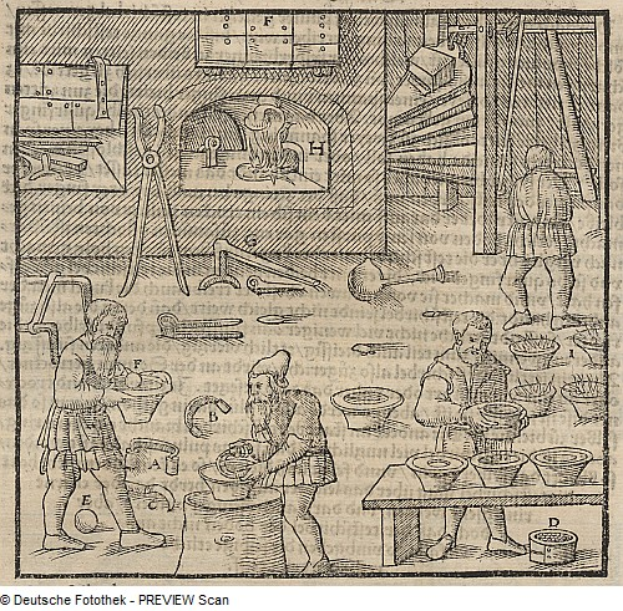 Eine Gravur einer Schmiedewerkstatt mit mehreren Personen um einen Tisch mit Schalen, Werkzeugen und Gegenständen herum und Text unten.