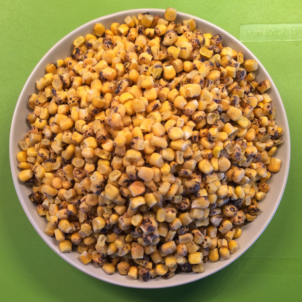 Ein weißer Napf voller Maiskörner wird gegen einen grünen Hintergrund gestellt, mit Text unten.