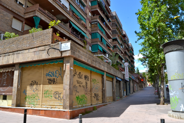 Eine Szene mit Gebäuden, die Fenster, grünen Kleidungsstücken, Geschäften, Schildern und umgebenden Bäumen und Pflanzen zeigen.