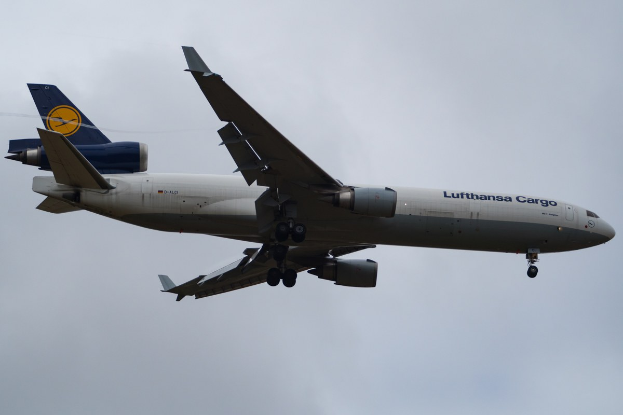 Ein Lufthansa Cargo Boeing 777-300ER im Flug, mit ausgefahrenen Flügeln und aktivierten Triebwerken, mit sichtbarem Text auf der Rumpfseite gegen einen bewölkten Himmel.