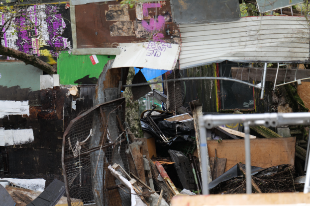 Ein Müllhaufen liegt vor einem mit Graffiti beschmierten Gebäude, umgeben von Bäumen und anderen Gegenständen.