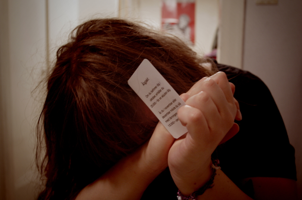 Eine Person hält eine Karte mit Text in der Hand und steht vor einem Plakat und einer Wand.