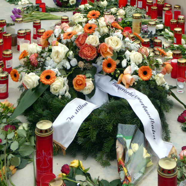 Ein Mahnmal in Berlin mit Blumen und Kerzen, die vor einer Wand auf dem Boden plaziert sind.