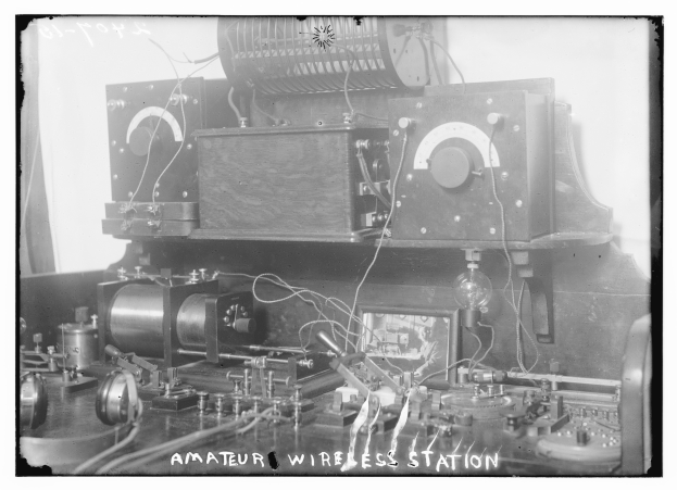 Ein altes Schwarz-Weiß-Foto einer Amateur-Funkstation mit verschiedenen elektronischen Geräten und Drähten, die miteinander verbunden sind, und Text am unteren Rand.