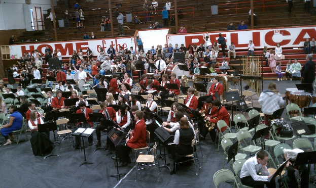 Eine Gruppe von Kindern sitzt auf Stühlen in einem Stadion bei einem Musikunterricht, mit sichtbaren Stadionplätzen im Hintergrund.