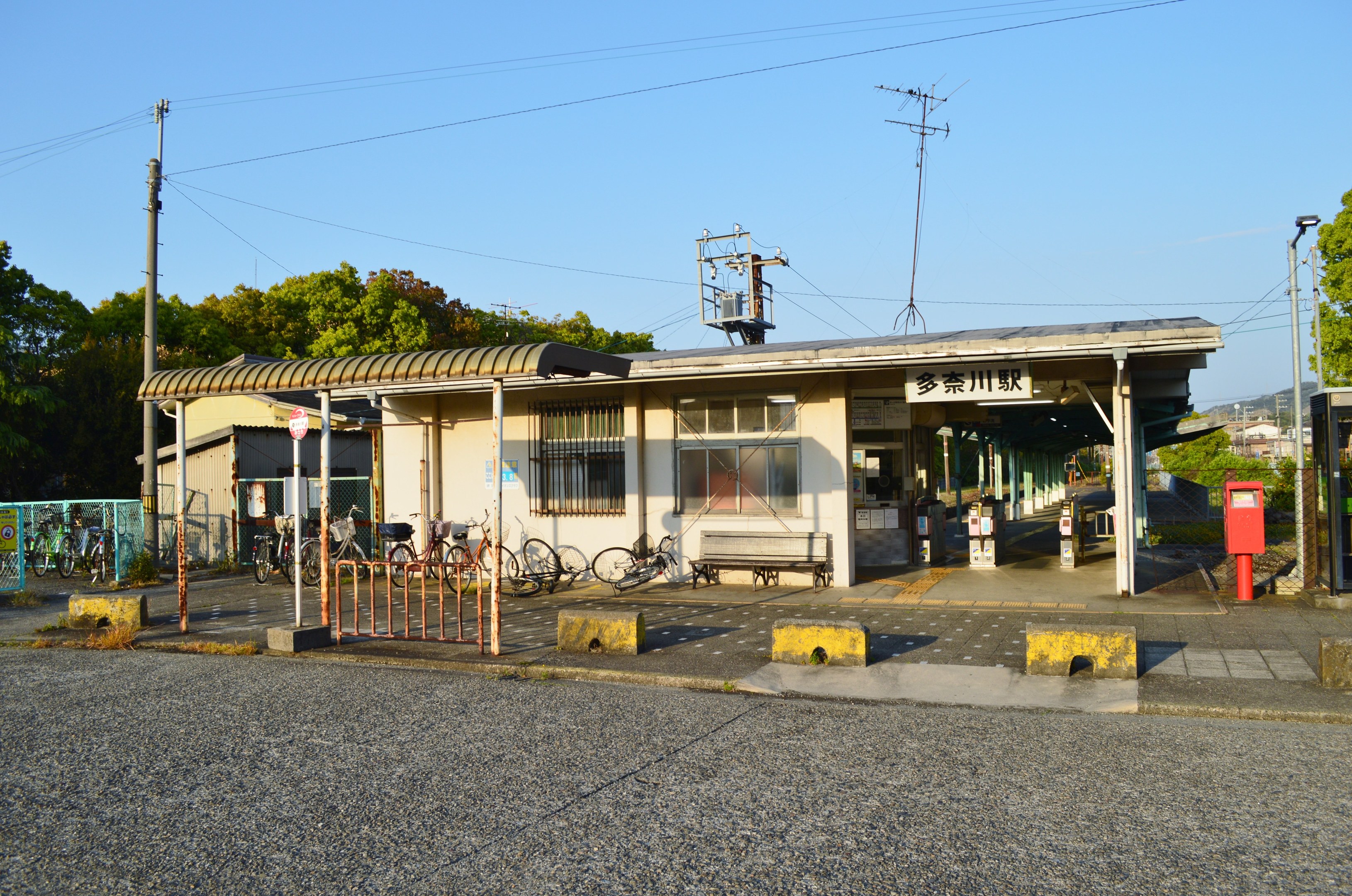 Fahrräder vor einem Bahnhof mit Häusern, Bäumen, Strommasten, Drähten und einem klaren blauen Himmel, mit einer Straße unten.