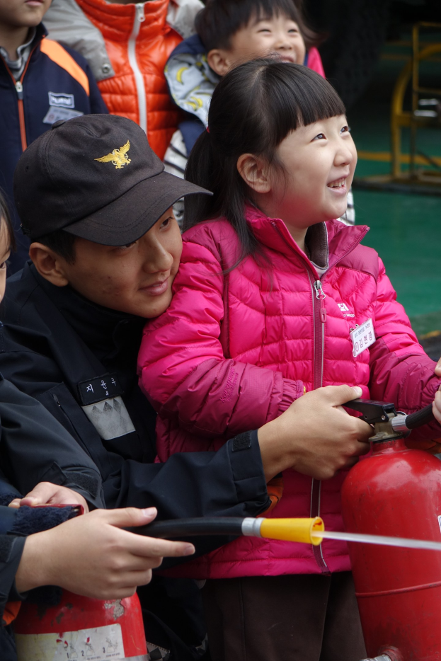 Kinder um einen roten Hydranten in einer Schulumgebung, einer hält ein Rohr.