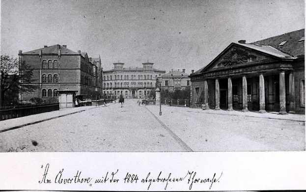 Ein Schwarz-Weiß-Foto einer Stadtstraße mit Gebäuden, Bäumen, Pfählen, Menschen und einer Straße, mit dem Text "1884 – die Königliche Akademie der Künste, London" unten.