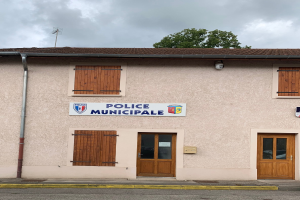 Polizeigebäude mit einem Schild, Fenstern, Türen, einer Namensschild, einem Rohr, einem Baum und einem bewölkten Himmel im Hintergrund.