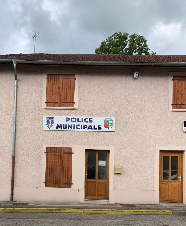 Polizeigebäude mit einem Schild, Fenstern, Türen, einer Namensschild, einem Rohr, einem Baum und einem bewölkten Himmel im Hintergrund.