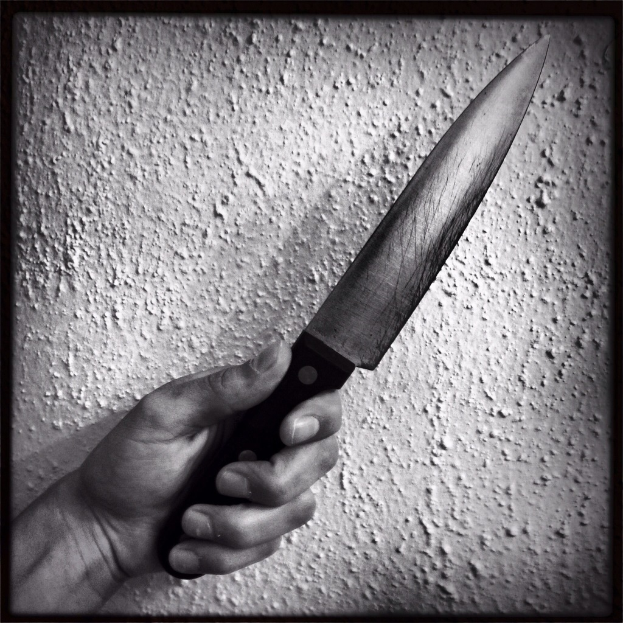 Ein Schwarz-Weiß-Bild einer Person, die ein Messer hält, mit einer Wand im Hintergrund.