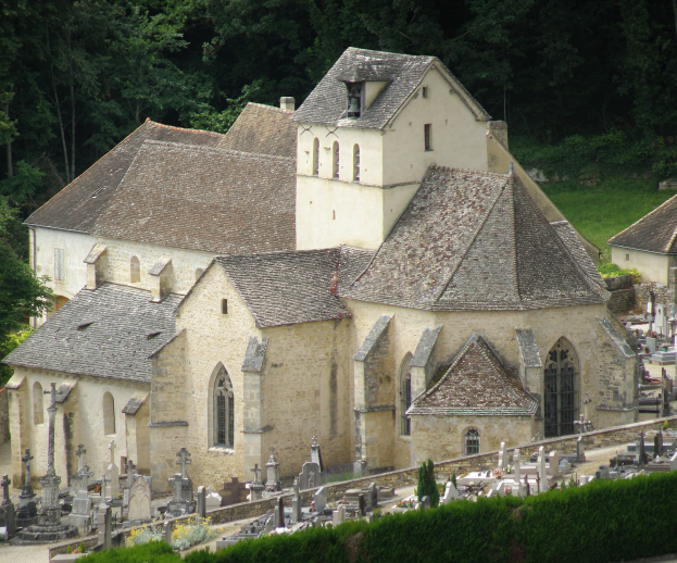 Eine alte Kirche mit einem Friedhof voller Grabsteine davor, umgeben von Häusern, Bäumen, Pflanzen und Gras, die eine friedliche und friedliche Atmosphäre schaffen.