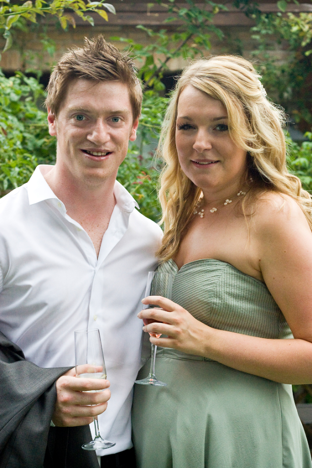 Ein Paar lächelt und hält Weingäser in der Hand, mit Bäumen im Hintergrund.