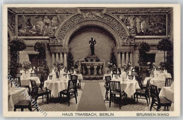 Schwarzes und weißes Foto eines alten Berliner Restaurantinnenraums mit Tischen, Stühlen, Blumenvasen, einer Statue im Hintergrund, geschnitzten Wänden, Pflanzen und Text unten.