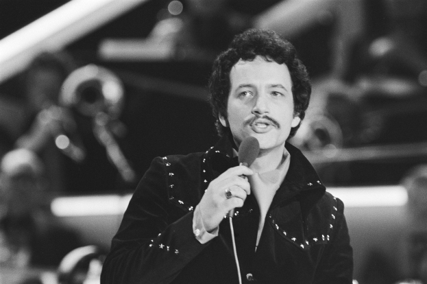 Ein als Elvis Presley identifizierter Mann hält ein Mikrofon während einer Live-Aufführung in einem Schwarz-Weiß-Foto mit unscharfem Hintergrund.