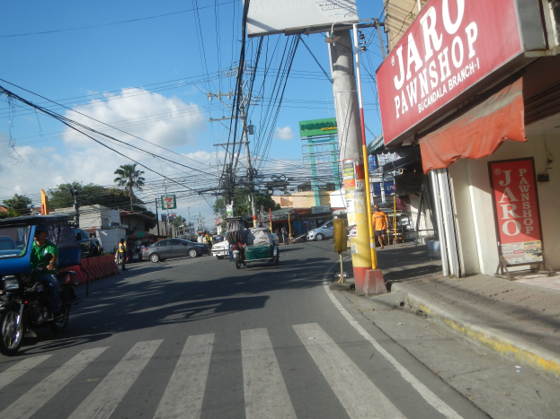 Eine belebte Stadtstraße mit Fahrzeugen, Fußgängern, Gebäuden und einem "Jaro Pfandleihhaus"-Laden auf der rechten Seite.