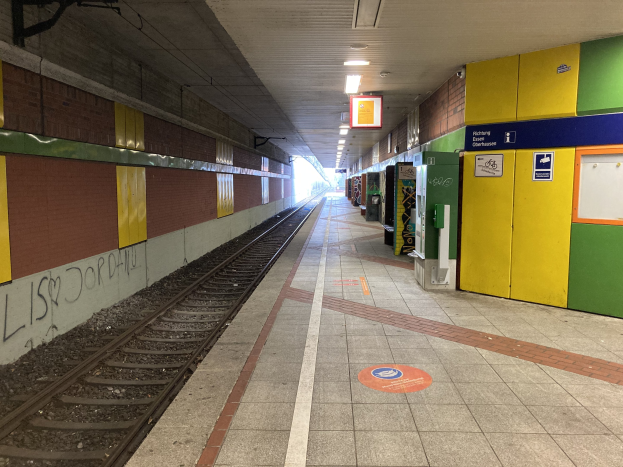 Ein Bahnsteig in Berlin Hauptbahnhof, Deutschland, mit einem Zug auf den Gleisen, beleuchtet von Deckenlampen, einer graffiti-bedeckten Wand auf der linken Seite und ein paar Gegenständen auf der rechten Seite.
