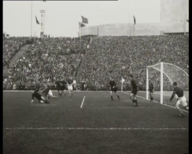 Schwarzes und weißes Foto des WM-Finales 1958 zwischen Manchester United und Liverpool, das Spieler auf dem Feld mit einem Torpfosten auf der rechten Seite und Zuschauern in den Rängen zeigt.