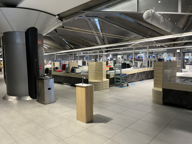 Ein geräumiger Raum im neuen Terminal des Frankfurter Flughafens, gefüllt mit Tischen, Stühlen, Maschinen und Säulen, mit wenigen Menschen und der Decke sichtbar.