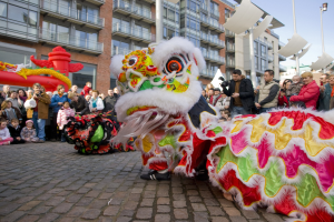 Eine Löwen-Tanzvorstellung während eines Chinesischen Neujahrsfestes in Amsterdam mit einer Zuschauermenge und Gebäuden im Hintergrund.
