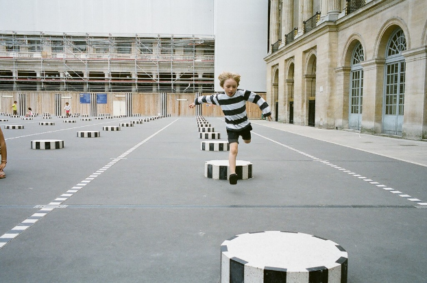 Ein Spielplatz mit vier Kindern, eines laufend auf dem Boden mit schwarzen und weißen Zementstufen, umgeben von einem Schulgebäude.