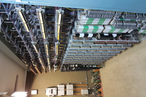 Ein geräumiger Raum voller numerous wires und elektronische Geräte auf dem Boden, mit einer Wand auf der linken Seite, wahrscheinlich ein Datenzentrum mit verschiedenen Servern und interconnected cables.