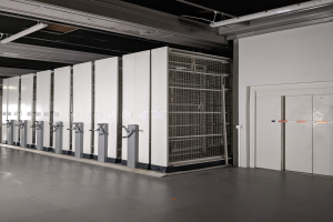 Ein großer Raum voller Numerous Server, mit einem Boden, einer Wand auf der rechten Seite und einer Decke mit Lampen oben, was auf ein Data Center hinweist.