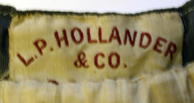 Ein Nahaufnahme eines Stoffetiketts mit dem Text "L.P. Hollander & Co" darauf, was wahrscheinlich ein Kleidungsstück von der Firma angibt.