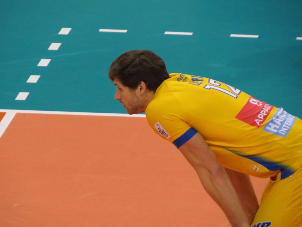 Eine professionelle Volleyballspielerin in einem gelben "Volleyball"-T-Shirt steht selbstbewusst auf einem Court und bereitet sich darauf vor, den Ball zu servieren.