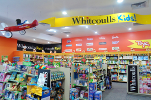 Ein hell erleuchteter Spielzeugladen mit Regalen und Gestellen voller verschiedener Spielzeuge, darunter ein Modellflugzeug, das von der Decke hängt.