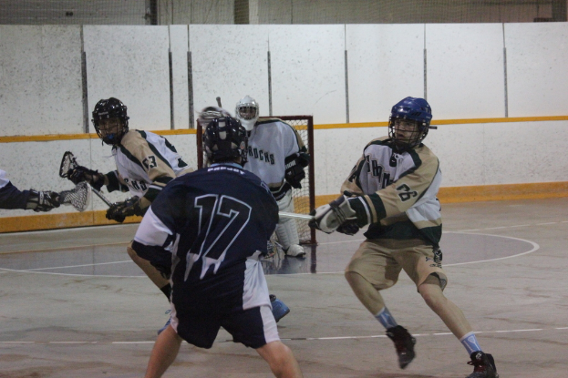 Menschen mit Helmen und Stöcken scheinen in einem Innenraum mit einem Netz im Hintergrund zu kämpfen.