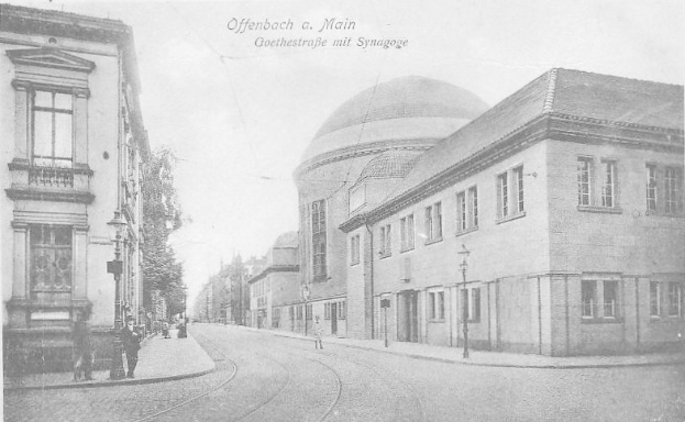 Schwarz-weiß-Foto einer Stadtstraße mit der Beschriftung "Offenbach a.M., Goethestraße mit Synagoge", das Gebäude, Laternenpfähle, Straßenlaternen, Bäume und Fußgänger zeigt.