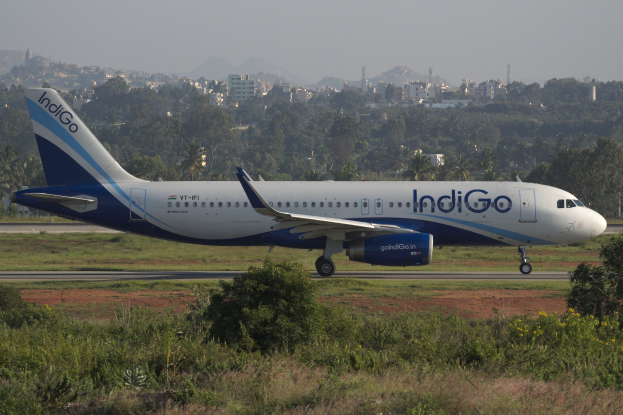 Indigo Airlines Airbus A320-200 auf der Rollbahn am Mumbai Airport mit Gras, Geb├Ąuden, Türmen, Bergen und Himmel im Hintergrund.