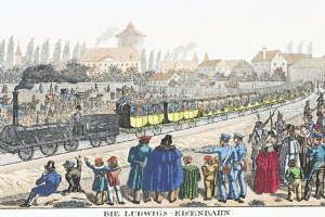 Eine Gruppe von Menschen steht in der Nähe eines Zuges auf den Schienen, mit einigen Passagieren im Zug und anderen außerhalb, vor einem Hintergrund aus Gebäuden und Bäumen, mit Text unten, der "Ludwigs-Eisenbahn, der erste Bahnhof in Deutschland" liest.