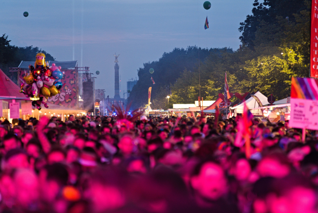 Eine große Menschenmenge auf einem nächtlichen Musikfestival mit bunten Lichtern, Ballons, Zelten, Bannern, Fahnen, Bäumen und einem sternenklaren Himmel im Hintergrund.