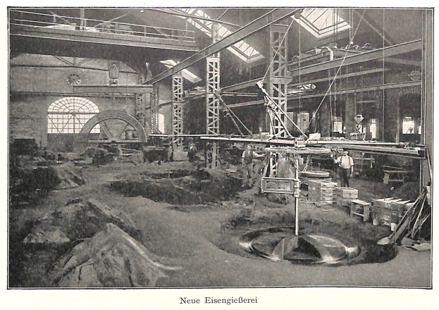 Schwarzes und weißes Foto eines historischen Fabrikinneren mit Arbeitern, die Maschinen bedienen, umgeben von Metallstangen und -rohren, beschriftet mit "Neue Eisengießerei, die erste Fabrik Deutschlands" unten.