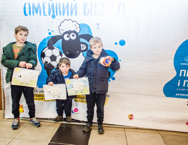 Drei Kinder halten Blätter vor einem Banner in den Händen.