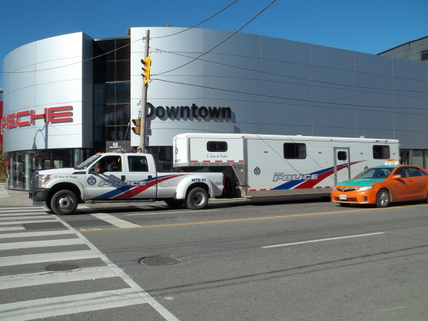 Polizeilaster vor einem Gebäude mit Text geparkt, mit einer Ampel und Kabeln im Vordergrund, Bäume und einen klaren blauen Himmel im Hintergrund.