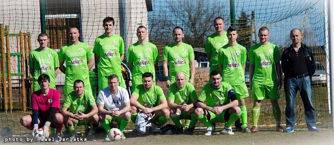 Gruppe von Männern in grünen T-Shirts auf einem Fußballfeld neben einem Torpfosten stehend, mit einem Fußball auf dem Boden.