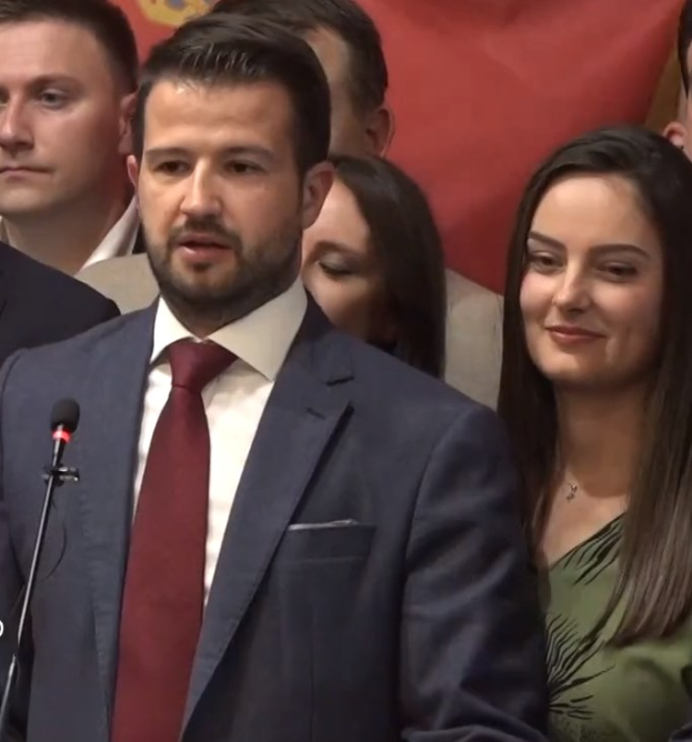 Ein Mann im Anzug spricht vor einem Publikum mit Mikrofon an einem Rednerpult, hinter einem Banner, wahrscheinlich über ein Regierungsozialmedienverbot.