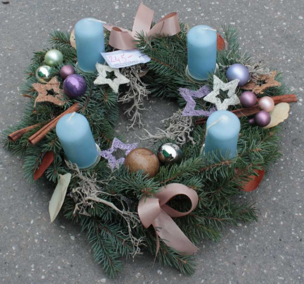 Ein beleuchtetes Weihnachtsgesteck mit Kerzen und Schmuck liegt auf dem Boden, gemacht aus Tannenzweigen, Blättern und Bändern.